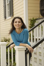 Hispanic woman leaning on railing of stairs to house