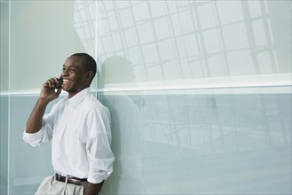 African businessman leaning against wall using cell phone