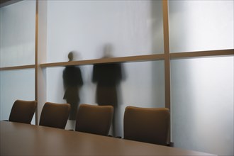 Silhouette of businesspeople through frosted glass wall