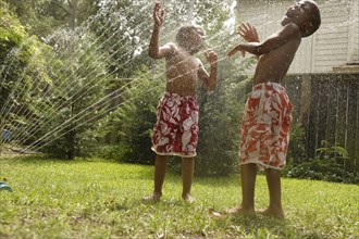 African American brothers playing in sprinkler