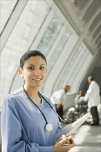 Hispanic nurse holding medical chart in corridor