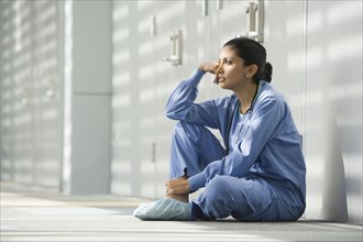 Hispanic nurse sitting on floor with head in hands
