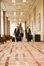 Multi-ethnic business people walking with suitcases in hotel