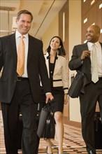 Multi-ethnic business people walking with suitcases down corridor