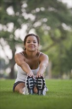 Mixed race woman sitting on grass stretching