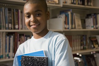 Mixed race boy holding books in library