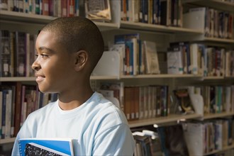 Mixed race boy holding books in library