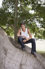 Hispanic teenager sitting on large tree trunk