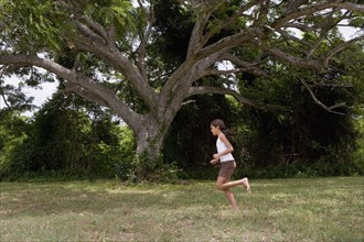 Hispanic girl running barefoot through grass