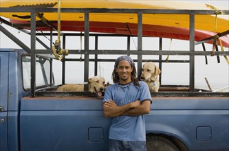 Hispanic man with dogs leaning against truck