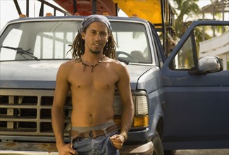 Bare chested Hispanic man leaning against front of truck