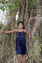 Hispanic girl leaning against mass of tree roots
