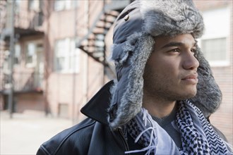 Mixed race man wearing fur hat and looking pensive