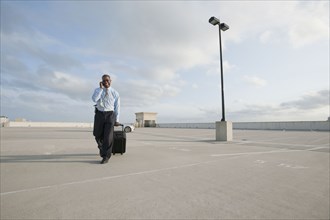 African businessman pulling luggage in parking lot