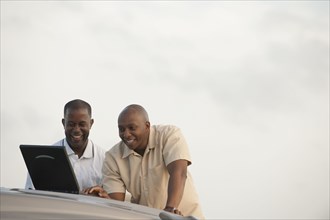 African businessmen using laptop on car hood
