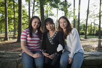 Mother and mixed race daughters sitting on stone wall