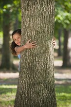 African American girl hugging tree trunk