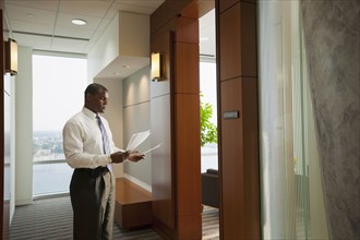 African American businessman holding paperwork in corridor