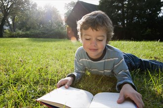 Mixed race boy reading book in grass
