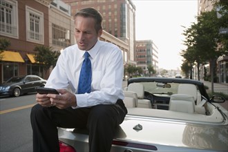 Caucasian businessman sitting on car text messaging on cell phone