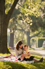 Caucasian mother reading story to daughter in park