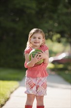 Caucasian girl holding watermelon on sidewalk