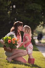 Caucasian mother holding flowers and kissing daughter