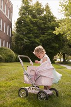 Caucasian girl dressed as princess playing with stroller