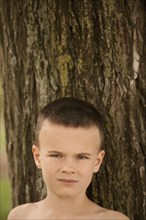 Caucasian boy leaning against tree trunk