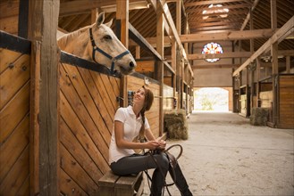 Caucasian girl sitting with horse in stable