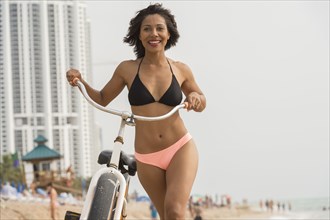 African American woman pushing bicycle on beach
