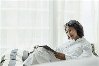 African American woman reading magazine near window