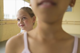 Girl peeking over shoulder of girl in ballet studio