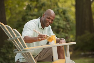 African American man painting chair in backyard
