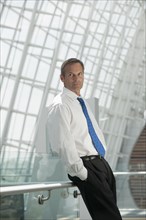 Caucasian businessman leaning on railing with hands in pockets