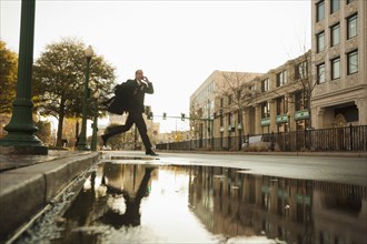 Caucasian businessman jumping over urban puddle