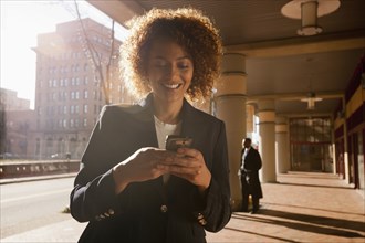 Mixed race businesswoman text messaging on cell phone