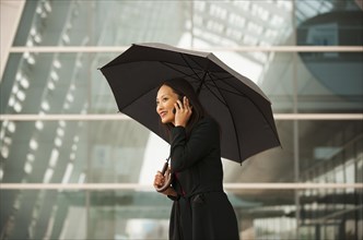 Asian businesswoman with umbrella talking on cell phone