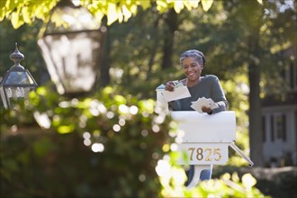 Mixed race woman reading mail at mailbox