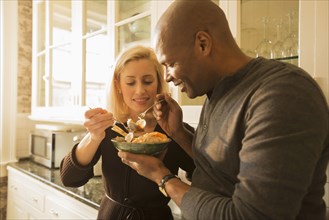 Couple sharing bowl of seafood stew in kitchen