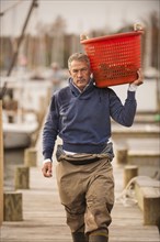 Caucasian fisherman carrying basket on dock