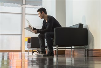Mixed race businessman reading papers in office lobby