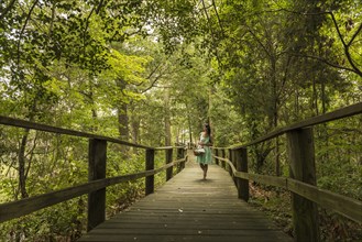 Hispanic woman walking on wooden footbridge in forest