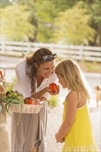 Mixed race mother and daughter smelling produce at farmers market