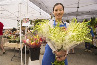 Asian clerk holding fresh flowers at farmers market