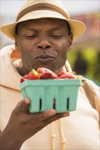 African American man examining basket of strawberries