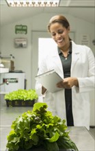Black scientist writing on clipboard near trays of green plants