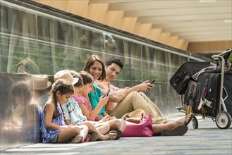 Family waiting on floor of airport using cell phones