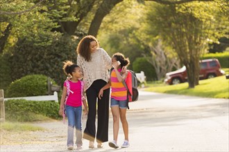 Mother walking in street with daughters wearing backpacks
