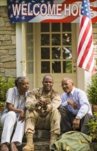 Soldier sitting on front stoop with parents and texting on cell phone